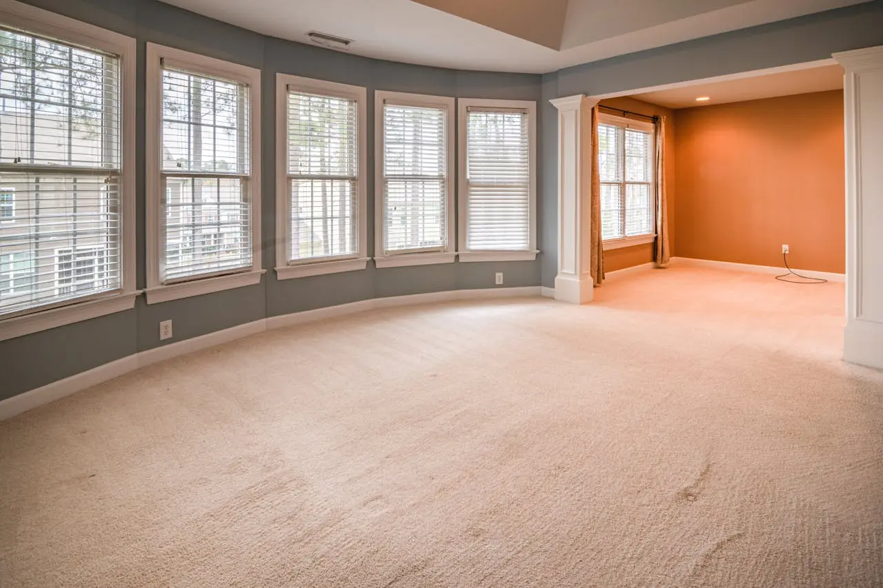 A large room with many windows and beige carpet.