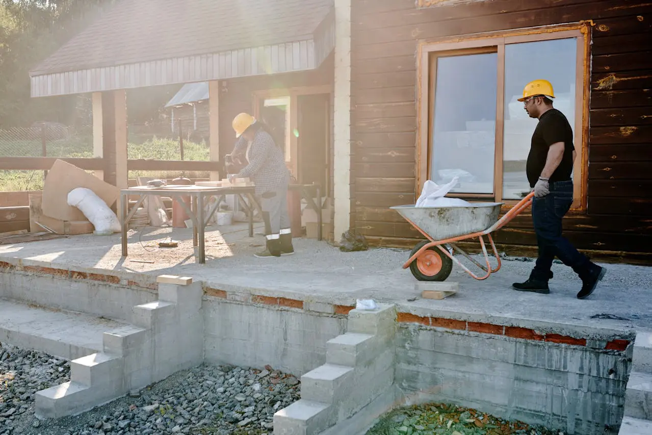 A man in yellow hard hat using a wheelbarrow.
